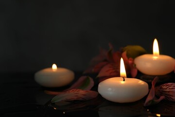 Burning candles and beautiful flowers on wet black table, closeup. Space for text