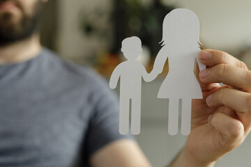 A man holds paper cutouts of a family, symbolizing family values, relationships, and parenthood.
