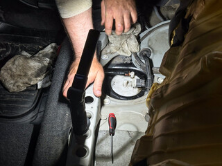 Mechanic checking automotive fuel system under rear seat, diagnostic tools and hands visible, professional car repair service and maintenance.
