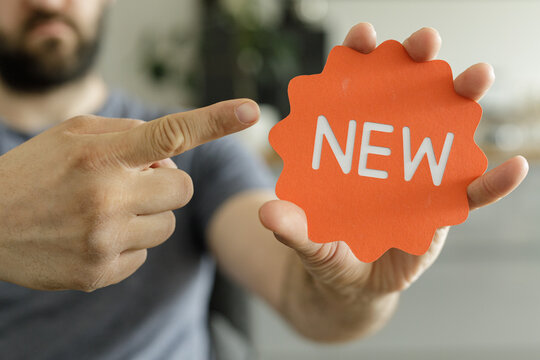 Close-up of a man's hand pointing at an orange 'NEW' sign.  Perfect for new product launches or announcements.