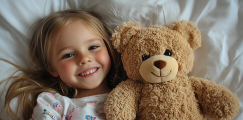 A happy little girl lying in a hospital bed, holding her teddy bear and smiling at the camera