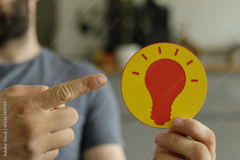 Poster a man points at a yellow circle with a red lightbulb, symbolizing ideas and innovation.