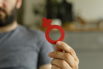 Close-up of a man's hand holding a red paper cutout of the female gender symbol.