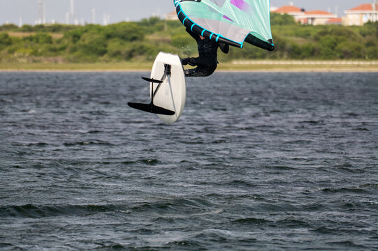 Close-up from a man in a black wet suit jumping with a wing foil at sunny weather in Netherland.