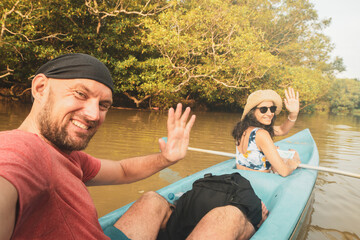 Happy caucasian tourist couple sit in double blue kayak and wave. Couple kayaks on calm waters...