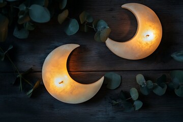 Moon-shaped soy candles glowing on a dark wooden table, scattered with eucalyptus leaves and soft flickering shadows