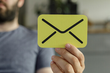 Close-up of a person holding a yellow card with an email icon.  Perfect for communication, contact,...