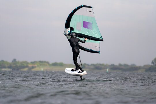 Close-up from a man in a black wet suit surfing a wing foil at sunny weather in Netherland in switch stand.