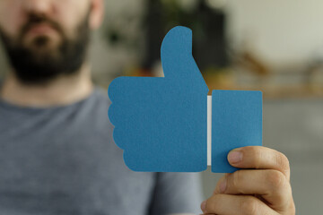Close-up of a man holding a large thumbs up sign, signifying approval or positive feedback.