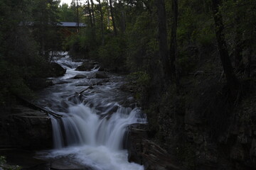 Slow shutter speed flowing creek water over rocks giving silken look with green foliage on sides and wooden bridge in background