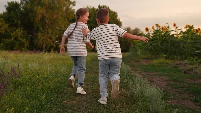 Children running together in nature, Kids playing in the countryside, Childhood friendship in the sunflower field, Summer evening outdoor activities, Happy children enjoying freedom, Boy and girl - Powered by Adobe