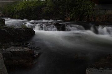 Low angle flowing creek water over rocks with dark green foliage in background