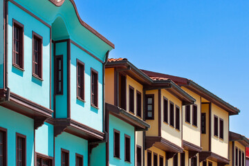 
Traditional Ottoman-era houses with distinctive turquoise and yellow facades line a street in Odunpazari, Eskisehir, under a clear blue sky. The vibrant architecture reflects the rich historical char