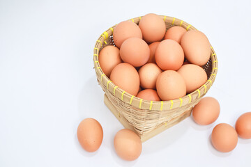 Brown eggs in a light brown woven basket on a white surface. Several eggs are scattered around the base of the basket