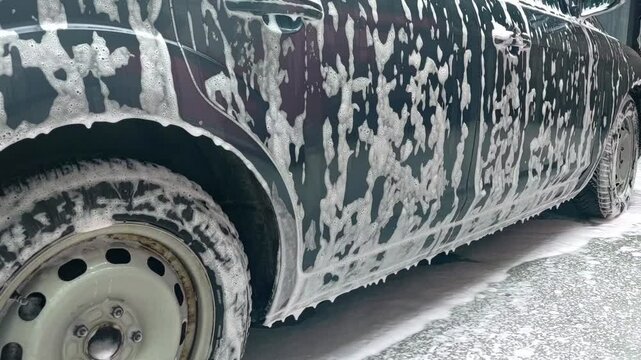 White foam covers car in outdoor wash process, auto detailing in progress