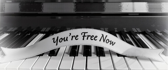 Piano keys with ribbon reading "You're Free Now" in monochrome setting  