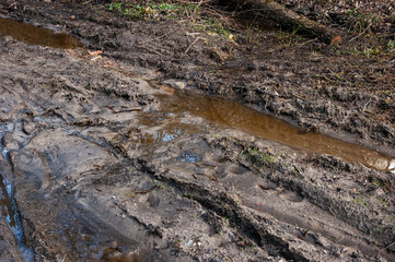 Very muddy dirt road with deep puddles and flowing water. The surface is churned up and full of footprints and tire tracks. The water is orange or brown from the clay soil.