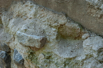 Concrete wall with granite pieces mostly crumbled. Cement between stones is cracked and worn, showing signs of age and decay.