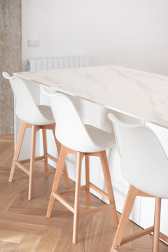 Encimera de cocina de m&aacute;rmol con sillas altas tipo taburete, en una casa reformada de dise&ntilde;o en tonos blanco y madera