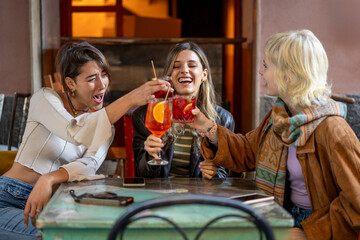 Young women friends toasting with spritz cocktails at an authentic bohemian bar in Italy.
