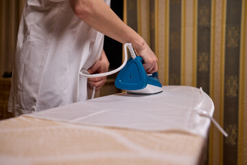 A person meticulously ironing clothes at home, ensuring all garments are neat and well cared for