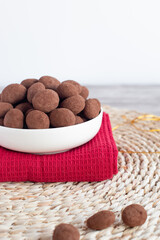 Chocolate almond truffles dusted with cocoa powder fill a white bowl on a red napkin and woven placemat, ready for a sweet treat