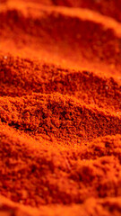 Deep red spice powder is spread across a surface, showcasing fine granules and a rich, earthy texture. The vibrant hue hints at its use in flavorful dishes and culinary creations.