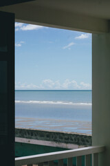 Fototapeta premium a view of the sea framed by an open doorway or window from what appears to be a room or balcony. The deep blue ocean stretches to the horizon under a bright sky with scattered white clouds.