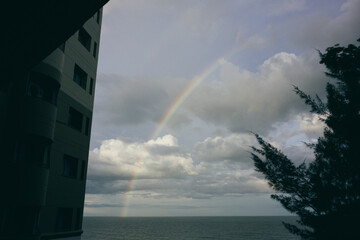 A vibrant rainbow arcs across a dramatic, cloudy sky, with its base seemingly touching the surface...