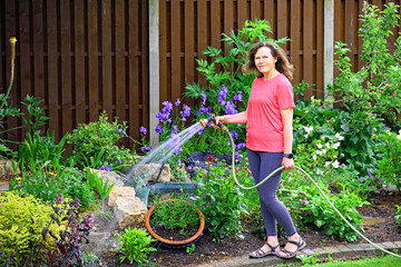 Woman watering flowers in a garden.