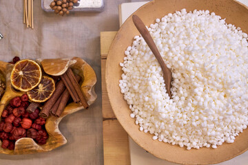 A creative workspace with tools, wax, dried flowers, and a ceramic bowl during the process of making a handmade candle. A cozy and aesthetic DIY moment