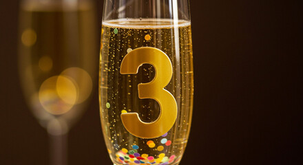 Close up of champagne glasses with bubbles and confetti with golden number three inside glass