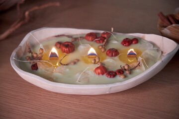 Close-up of a lit handmade candle in a ceramic bowl with wooden wicks. Decorated with dried flowers and cozy autumn details, this warm, rustic composition evokes a sense of relaxation, aromatherapy