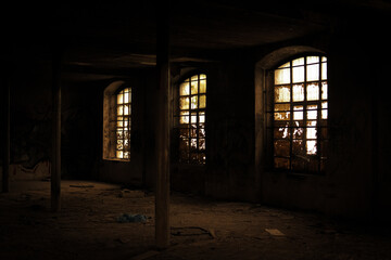 Dark interior of an abandoned building with broken windows. Light filters through the dirty glass,...