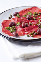 Slices of beef carpaccio with olives and capers. Close up.	