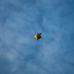 A bright helium balloon shaped like a star gently rises against a clear sky, bringing a sense of...