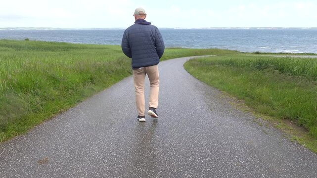 Mors, Denmark A man walks down a road towards the Limfjord on a rainy windy day. 