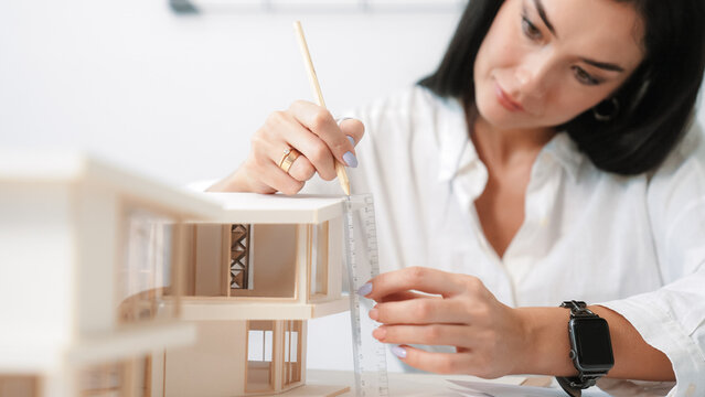 Closeup portrait image of professional young beautiful engineer architect using triangular scale measures house model with focusing at modern office. Business creative design concept. Immaculate.