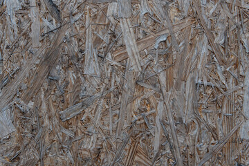 Close-up of raw chipboard (particle board) surface. Visible wood chips and compressed structure form a natural industrial texture. Ideal for backgrounds and design.