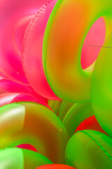 Close-up of stacked neon pink and green inflatable swim rings glowing under bright sunlight. Vivid summer colors and textures create a bold, abstract visual composition.
