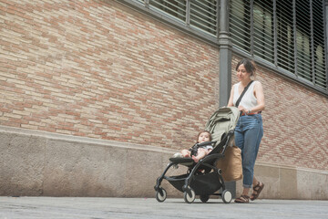 Mother walking with baby stroller along urban street in Barcelona