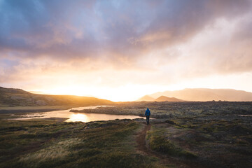 Lone traveler walks through the mossy lava fields of Berserkjahraun toward Selvallavatn lake, bathed in golden sunset light on Icelands Snaefellsnes Peninsula © Fauren
