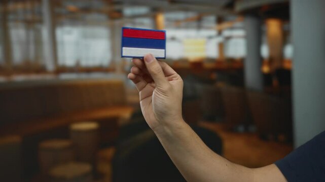 Man holding embroidered russia flag patch indoors at a coffee restaurant.