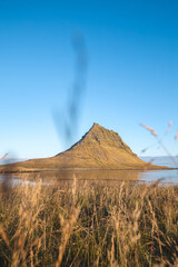 Iconic peak of Kirkjufell rises sharply on Snaefellsnes peninsula Iceland bathed in golden sunlight...