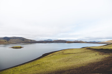 Serene volcanic lake with a tiny mossy island sits in the Icelandic highlands, surrounded by rugged...