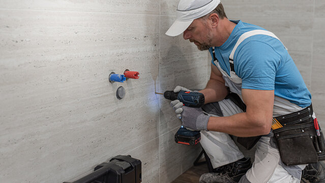 Installation of bathroom furniture. The plumber is drilling into the gres tile. He works with cordless drill with special drill.