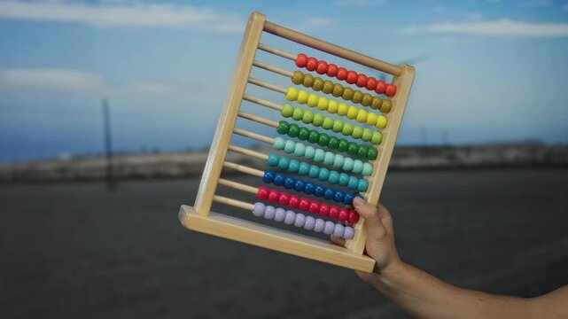 Hand holding colorful abacus outdoors in front of windmill and landscape during day.
