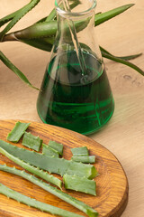 Laboratory flask with medicinal aloe vera juice on a wooden background. The concept of using natural ingredients in medicine. Vertical photo