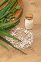 Homeopathic treatment - Homeopathic balls poured from a glass bottle into a petri dish on the background of an aloe vera flower. The concept of using natural plants in homeopathy. Vertical photo