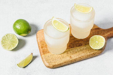 Refreshing lime cocktails on wooden board. Two glasses of citrus hard seltzer with ice cube and...
